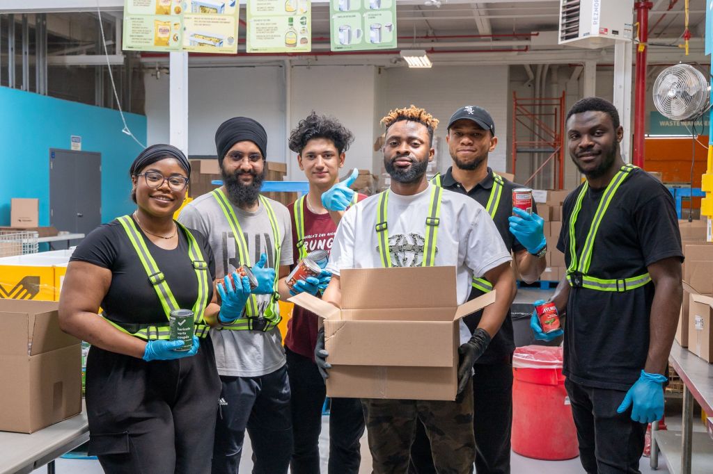 Group of diverse volunteers packing food at a warehouse, wearing safety vests and gloves.