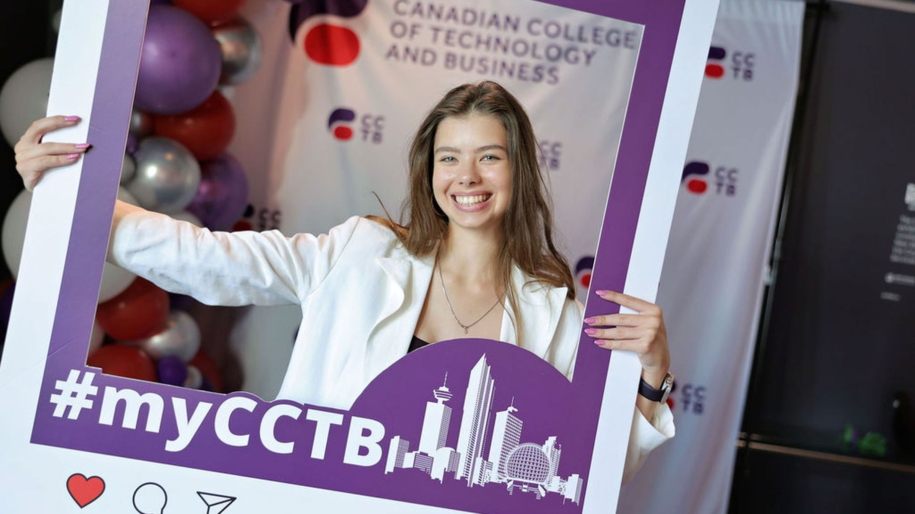 A smiling student holding an Instagram frame whilst posing for a photo.