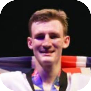 Smiling athlete with a flag (appears to be French) draped over their shoulders against a dark background.