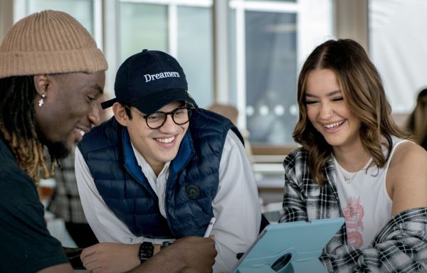 Group of students looking at a tablet screening and smiling.