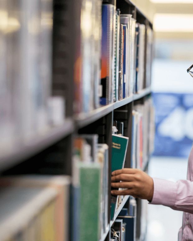 A person selecting a book from a tall bookshelf in a quiet library.