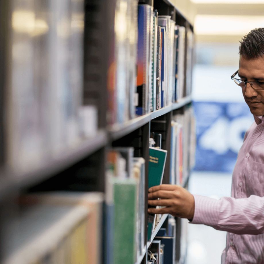 A person selecting a book from a tall bookshelf in a quiet library.