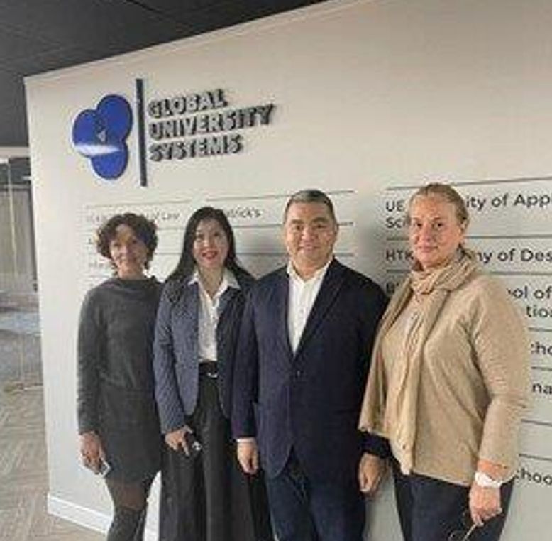 Four people standing in front of a Global University Systems logo and directory wall.