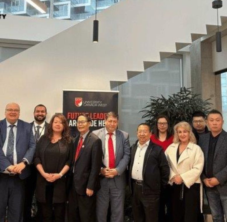 A group of professionals posing at a University Canada West event, with a banner reading 'Future Leaders Are Made Here' in the background