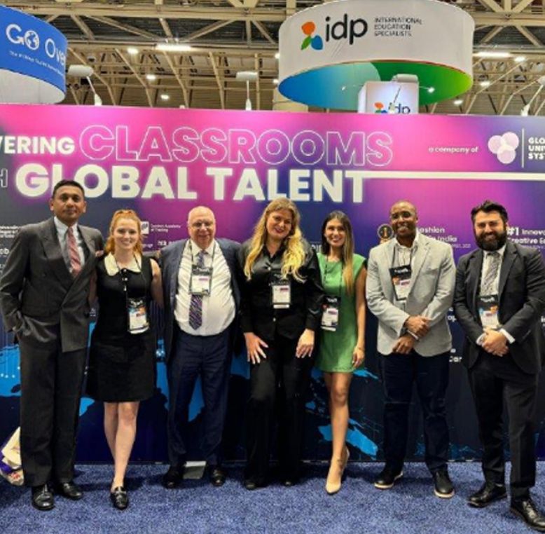 A group of people standing in front of Global University Systems signage at NAFSA 2024.
