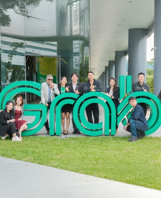 A group of people surrounding a large 'Grab' sign outside offices.