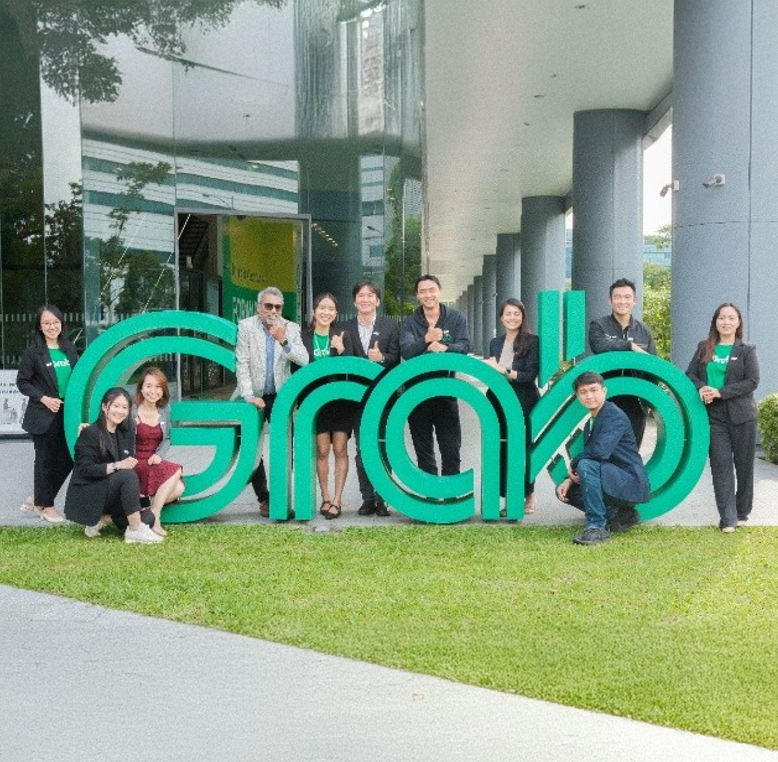 A group of people surrounding a large 'Grab' sign outside offices.