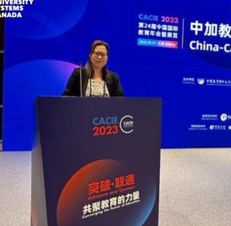 Speaker at the CACIE 2023 conference stands at a podium with a blue backdrop displaying 'China-Canada' education collaboration