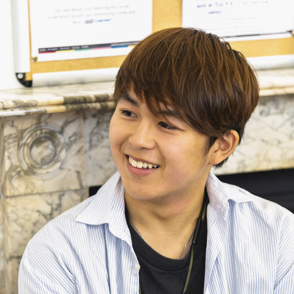 Student smiling at the camera, wearing a shirt, with his chin and jaw visible. The background shows an indoor wall.