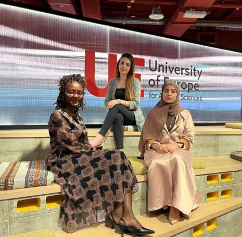 Esther Wairimu Kamau, Heba Abedalbaki, and Hadil Aziz Saeed Ahmed Alzeqri seated together in the auditorium at the University of Europe (UE).