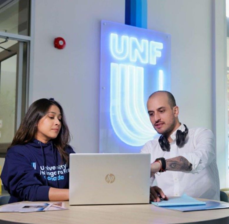 Two UNF students looking at a laptop in a classroom