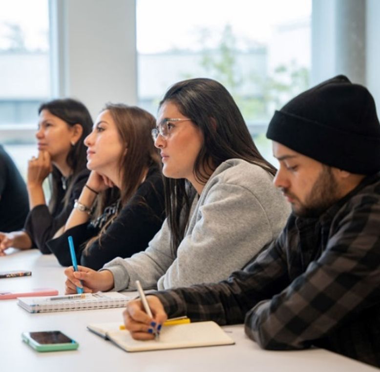 Four students listening to their teacher in a classroom.