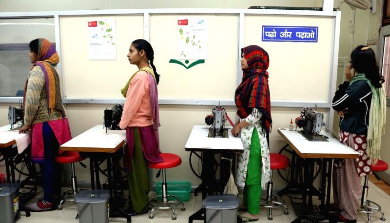 Two female Tihar Jail inmates standing up in front of sewing machines.