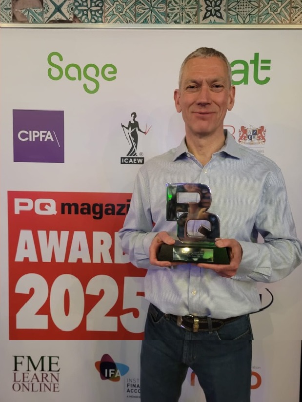 Man in light blue shirt holding a trophy at PQ magazine Awards 2025, standing next to red and black 'WINNER' banner with sponsor logos in background.