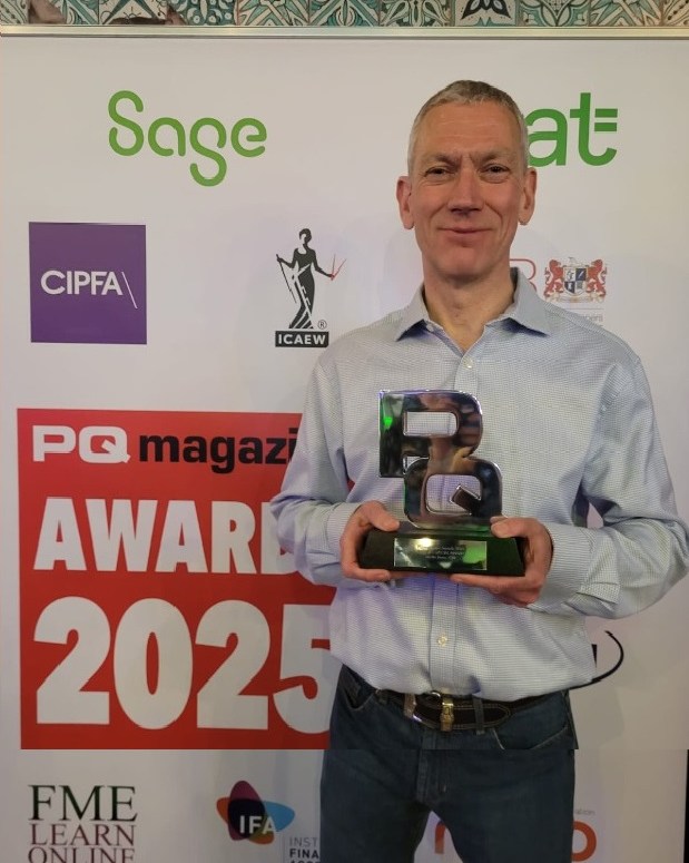 Man in light blue shirt holding a trophy at PQ magazine Awards 2025, standing next to red and black 'WINNER' banner with sponsor logos in background.