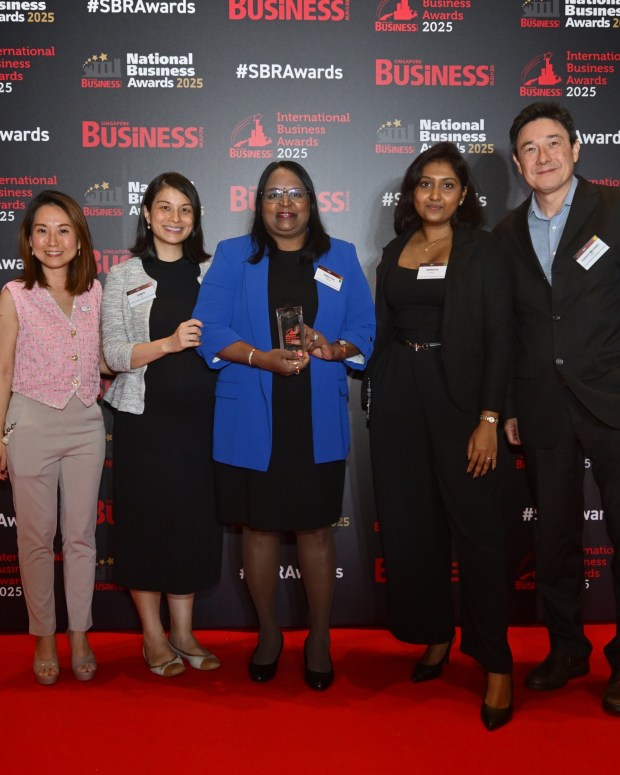 Five people posing together at the National Business Awards 2025, with one person in a blue blazer holding an award trophy, standing in front of a branded backdrop with red carpet.