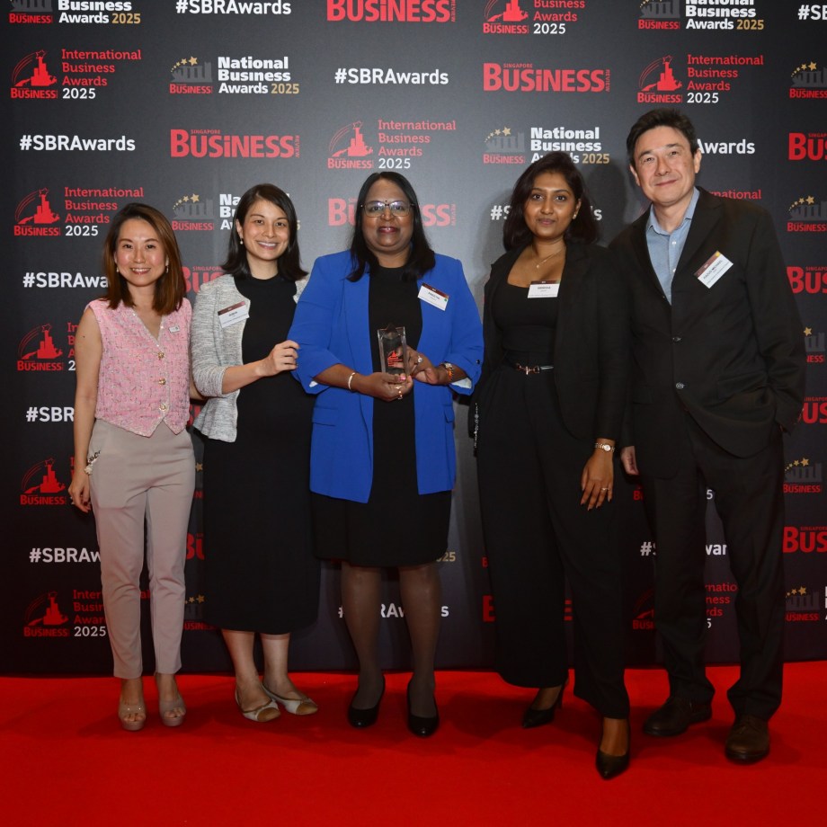 Five people posing together at the National Business Awards 2025, with one person in a blue blazer holding an award trophy, standing in front of a branded backdrop with red carpet.