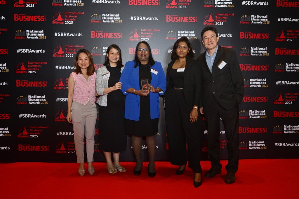 Five people posing together at the National Business Awards 2025, with one person in a blue blazer holding an award trophy, standing in front of a branded backdrop with red carpet.