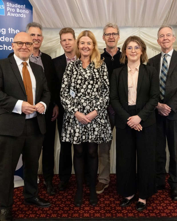 Group of seven people in business attire posing at LawWorks Student Pro Bono Awards event, standing in front of blue branded backdrop.