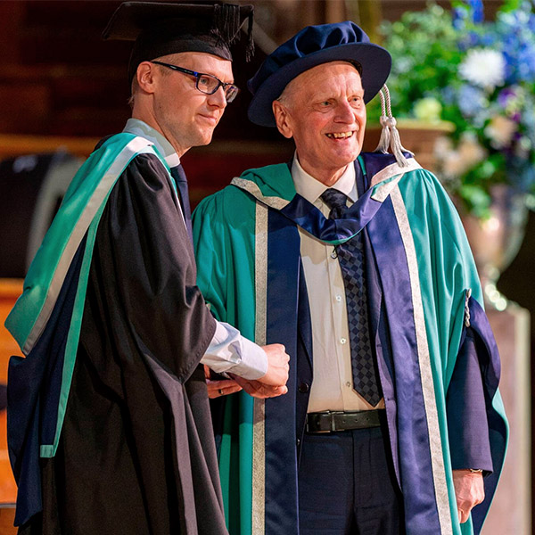 Two people in academic regalia shake hands at a graduation ceremony.