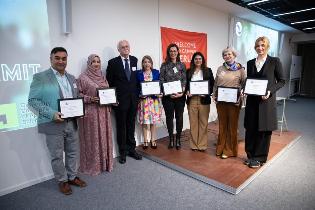 Group of certificate recipients and presenters posing with awards at university event with 'Welcome to Campus Berlin' banner.