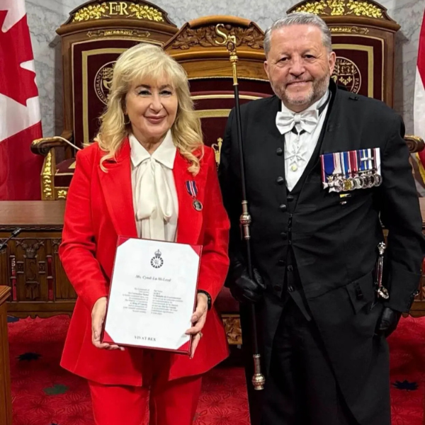 Image of Cyndi McLeod, CEO of GUS Canada and man in formal attire with military medals holding certificate in ornate chamber with Canadian flags.