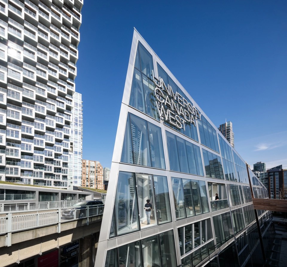 Modern glass building of University Canada West in downtown Vancouver, surrounded by high-rise architecture under a clear blue sky.