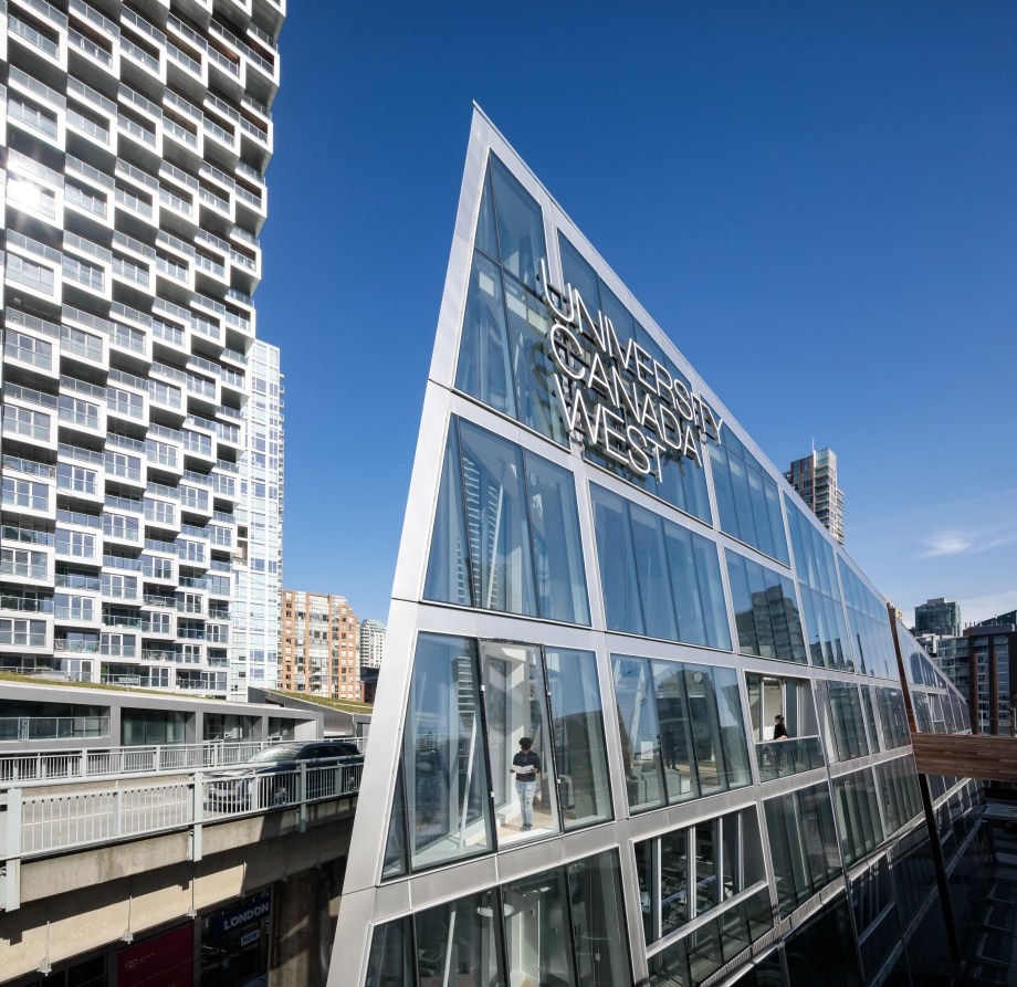 Modern glass building of University Canada West in downtown Vancouver, surrounded by high-rise architecture under a clear blue sky.