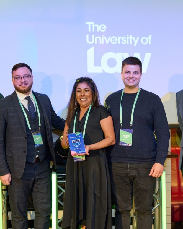 Five people with conference badges posing for group photo with The University of Law logo in the background.