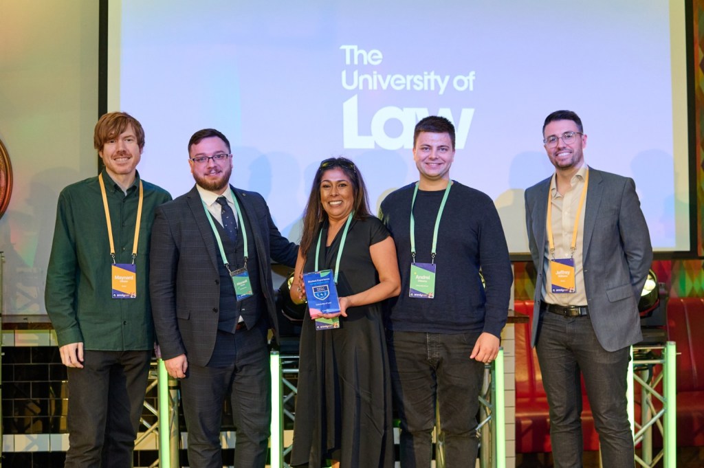 Five people with conference badges posing for group photo with The University of Law logo in the background.