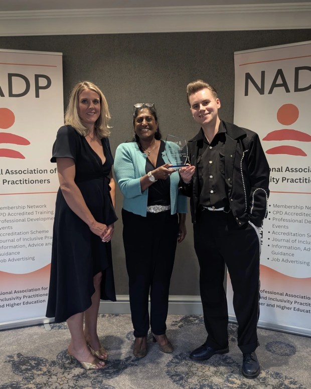 Three people posing with an award at an NADP conference, standing between two organisational banners.