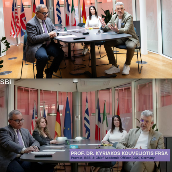 International meeting with four people at conference table surrounded by multiple country flags.
