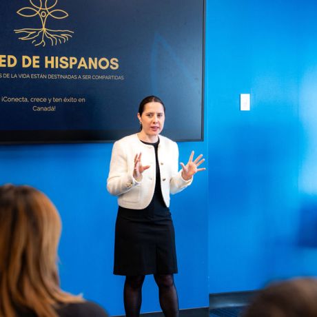 Woman in white blazer presenting to audience at La Red de Hispanos networking event.