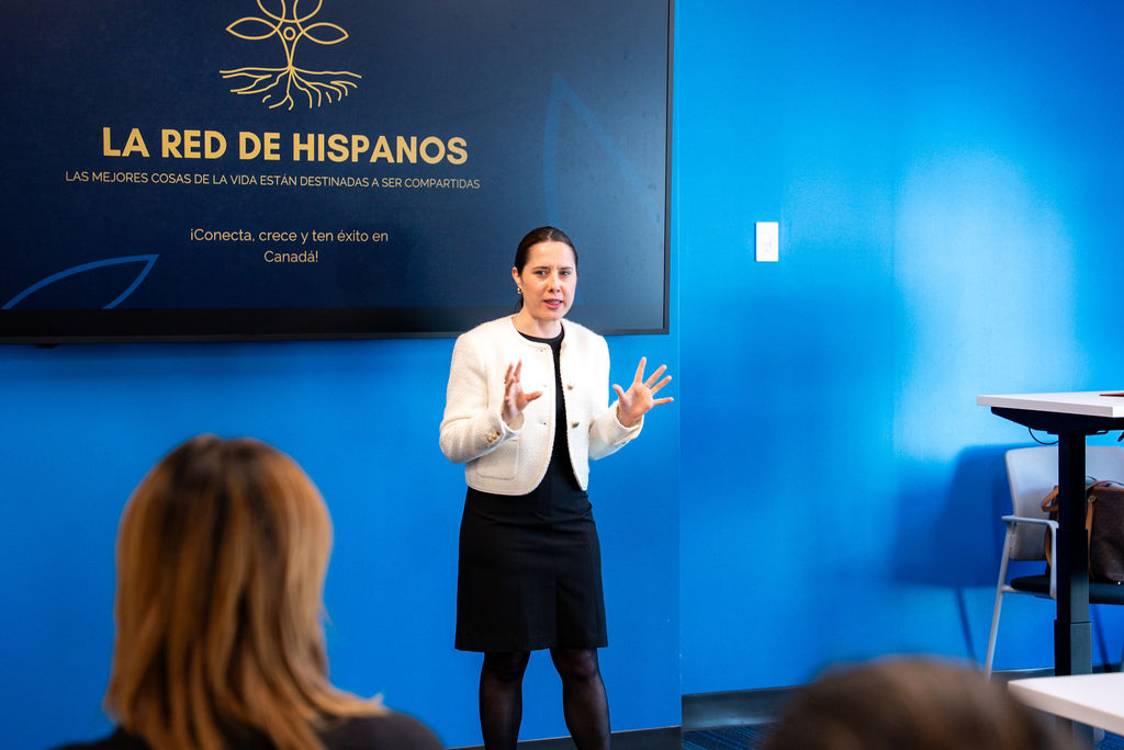 Woman in white blazer presenting to audience at La Red de Hispanos networking event.