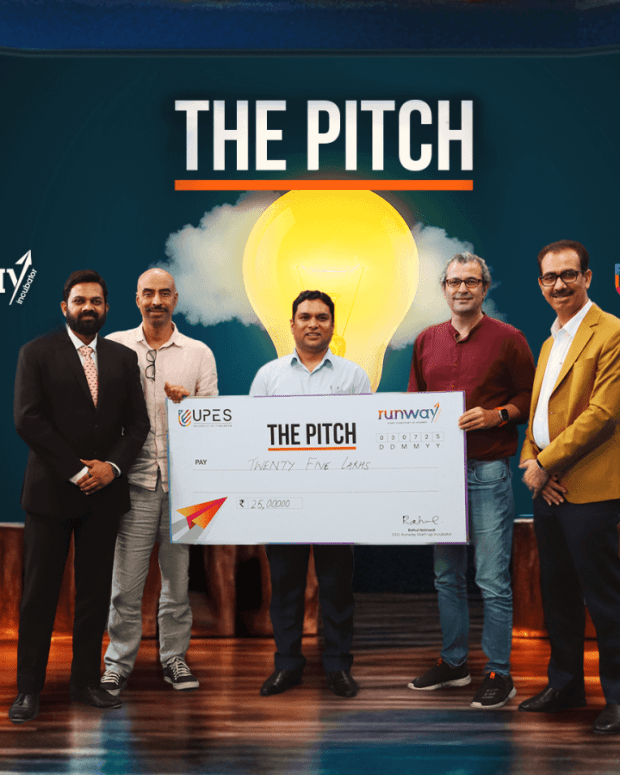 Five men holding large ceremonial check at 'The Pitch' startup competition event with runway and UPES branding.