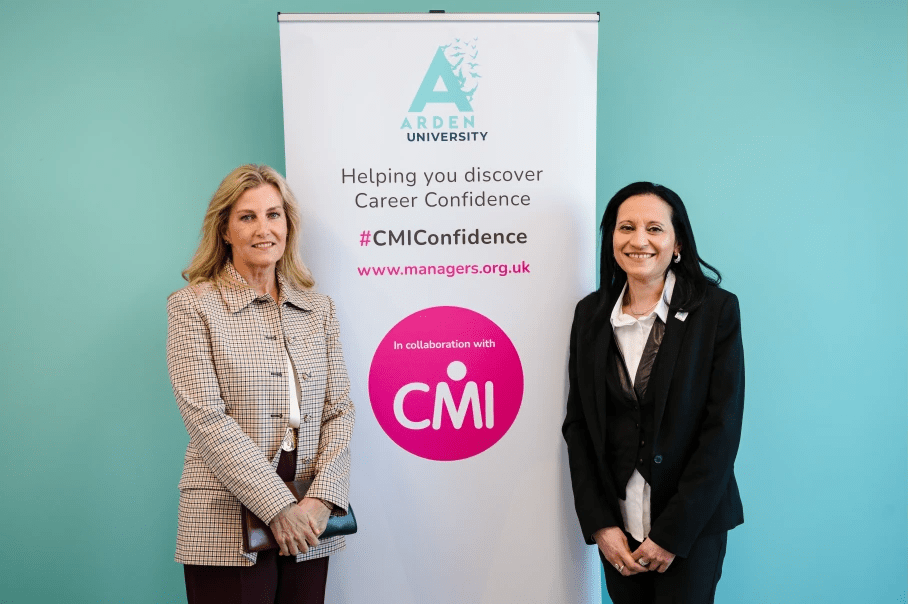 The Duchess of Edinburgh standing with an Arden University staff member in front of an Arden University and CMI banner against a turquoise wall.