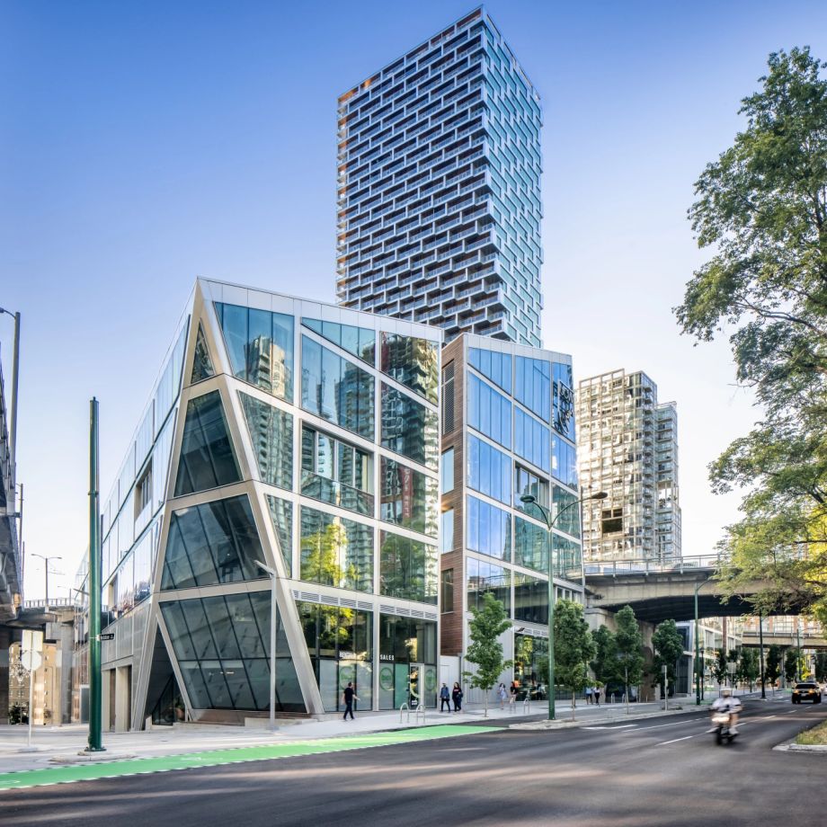 Modern glass building of the UCW campus in Vancouver, with high-rise towers and trees nearby.