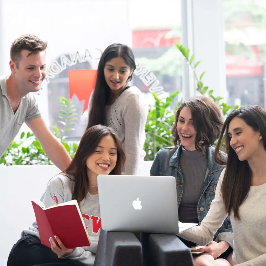 Five students smiling and working together on a laptop.