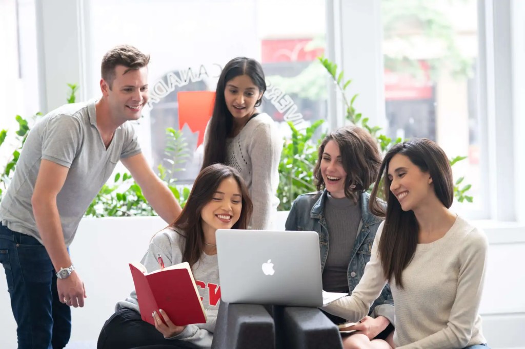 Five students smiling and working together on a laptop.