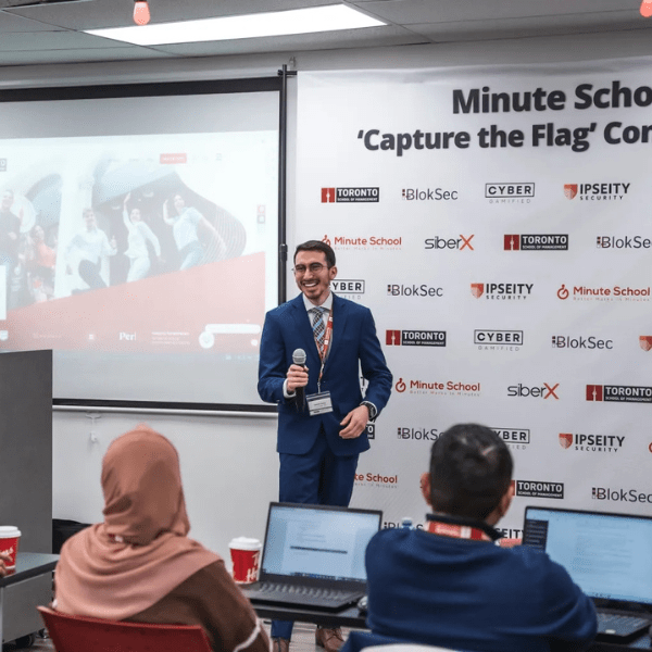 Speaker in suit speaks to participants working on laptops.