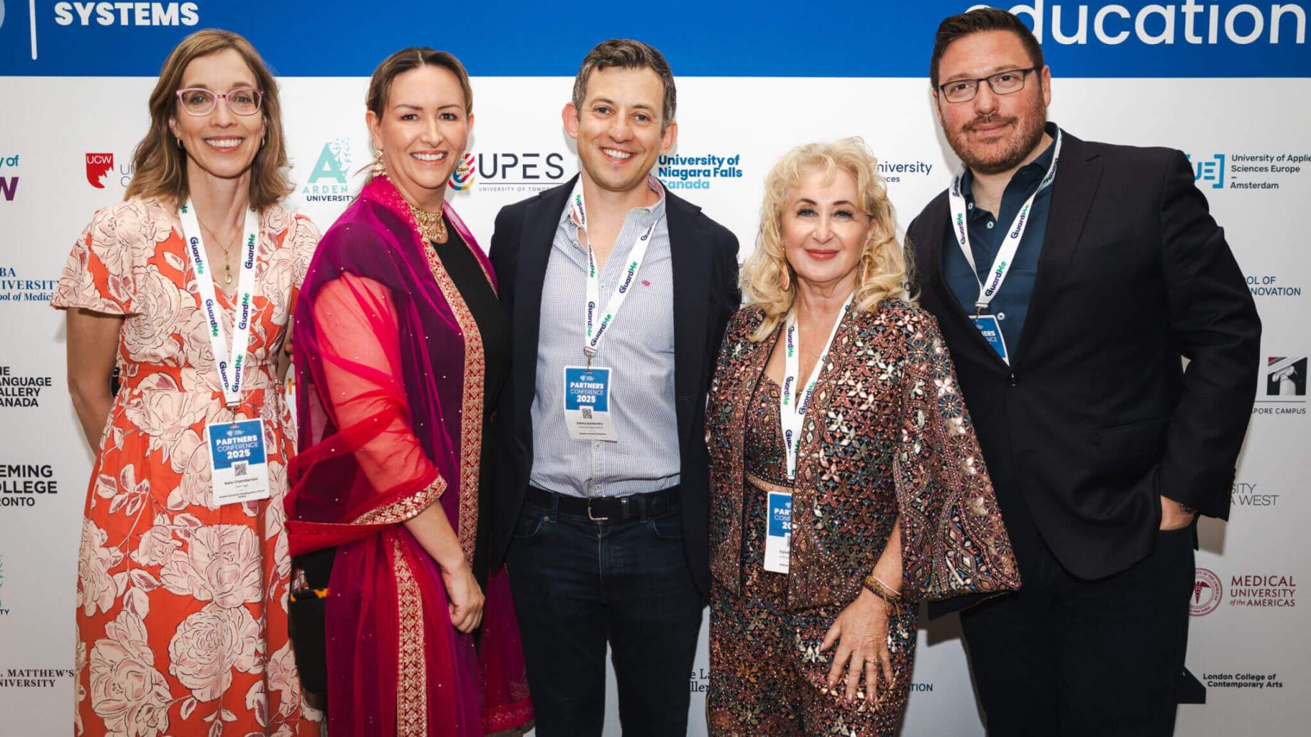 Five attendees pose and smile together in front of a Global University Systems conference backdrop.