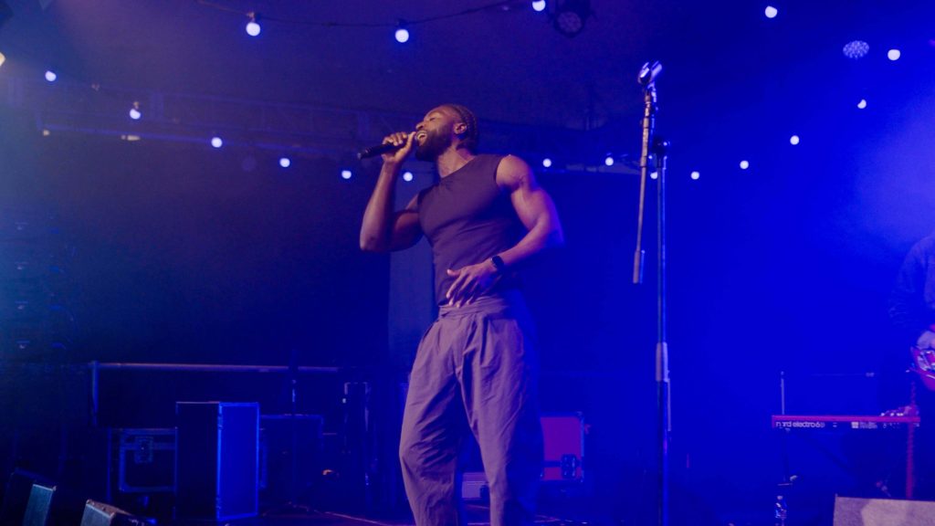 Person performing on stage under blue lights, holding a microphone with equipment nearby.