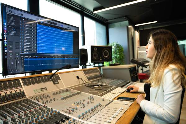 Person working at an audio mixing console in a recording studio with editing software on screen.