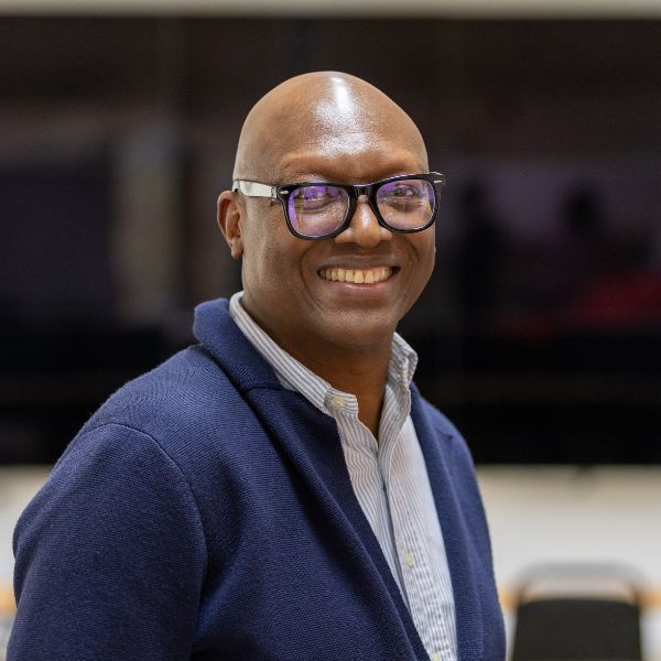 Person in glasses and a navy sweater smiles indoors.