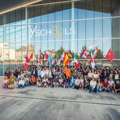 Group photo of Y SCHOOLS students and staff gathered outside the institution’s modern campus building, holding international flags to celebrate diversity and global community.