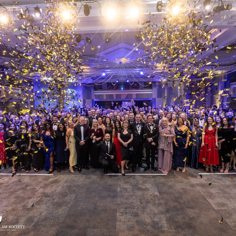 Large group of attendees in formal evening wear celebrating at the Birmingham Law Society Awards event, with gold confetti falling under bright stage lights in a banquet hall.